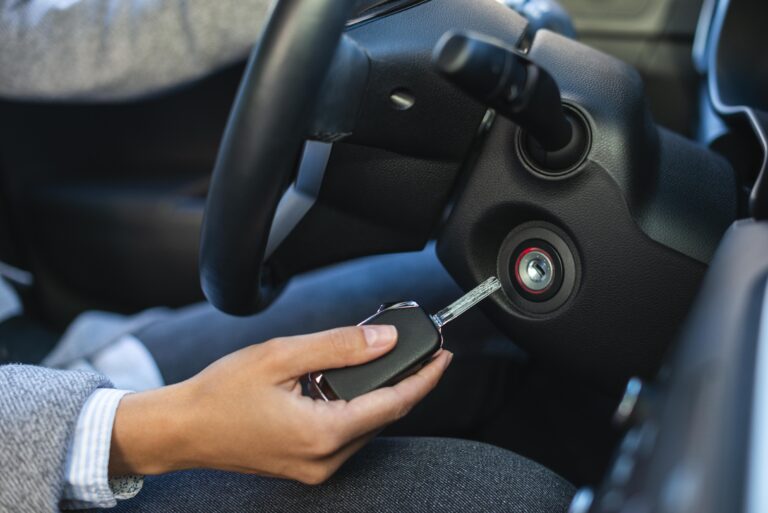 Řidič drží klíč od auta u zapalování; postup při nefunkčním klíči po pádu nebo vybití baterie, včetně kdy volat autozámečníka.